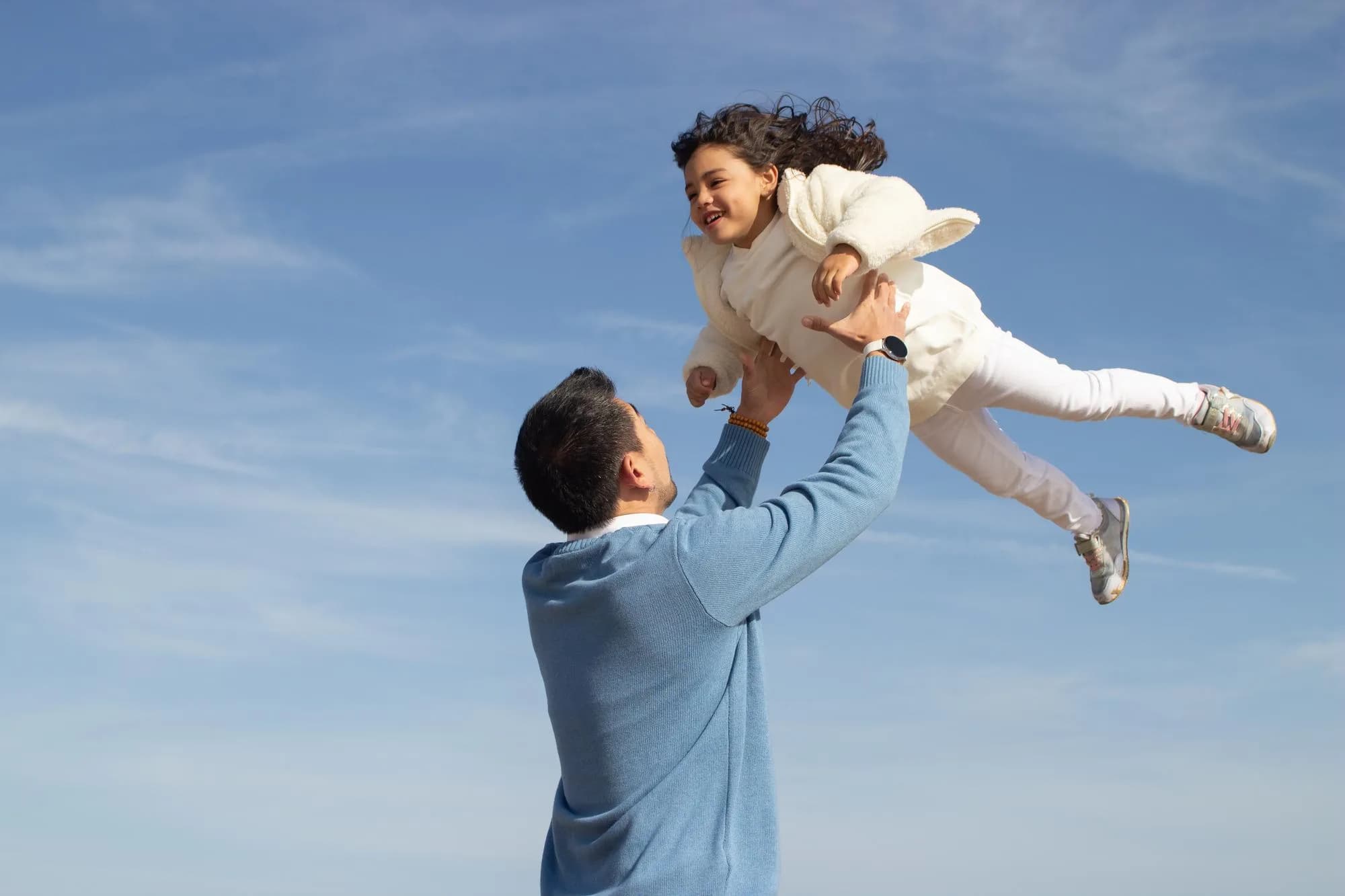 A parent lifting their child against a bright sky