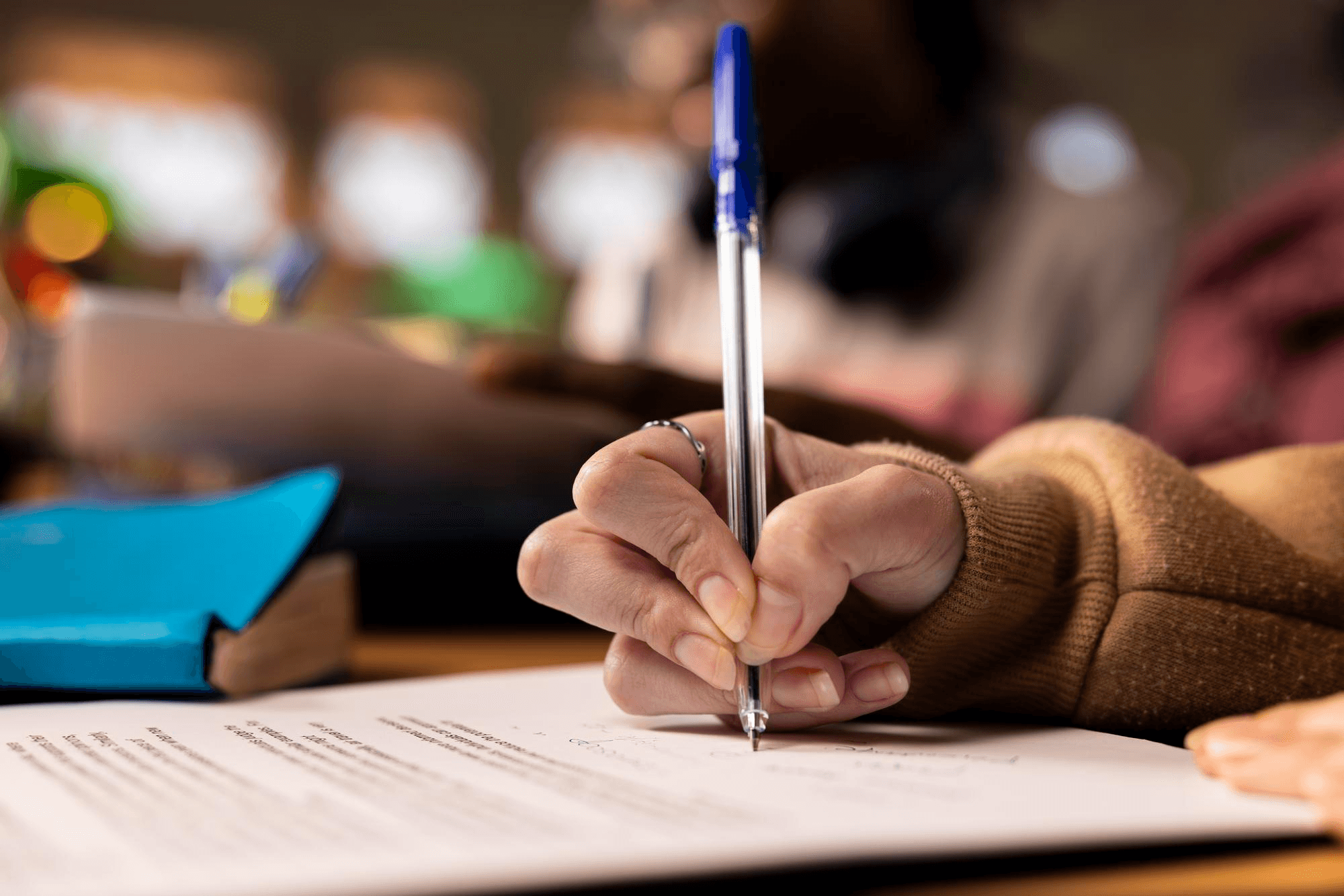 A hand signing a document with a blue pen